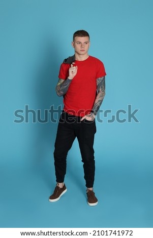 Young man with tattoos on light blue background