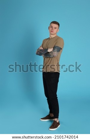 Young man with tattoos on light blue background