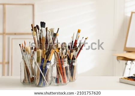 Different paintbrushes on white table in studio, space for text. Artist's workplace