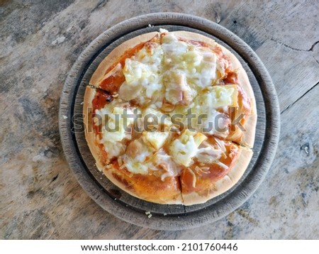 On an ancient wooden table Hawaiian Pizza is served on a wooden platter.