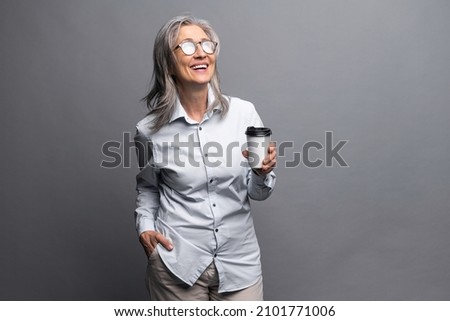 Morning coffee to go. Charming senior woman in formal wear standing with paper cup of hot drink isolated on gray, preparing to good working day. Mature business lady takes a coffee break Royalty-Free Stock Photo #2101771006