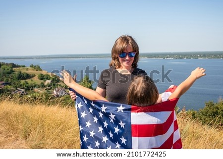Happy young woman with daughter and american flag playing in nature on a sunny day.