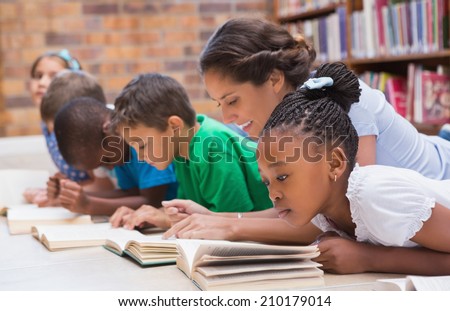 Cute pupils and teacher lying on floor in library at the elementary school Royalty-Free Stock Photo #210179014