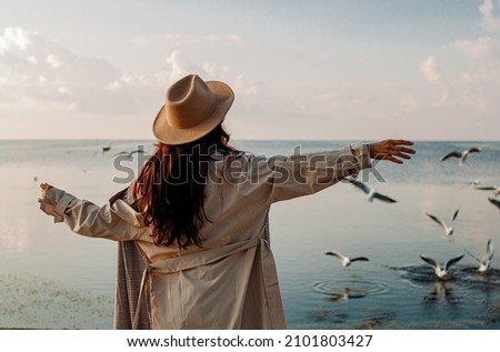 Young woman feeds seagulls at winter sea beach. Amazing coastline scene with girl. Concept of freedom, travel, flying. Lifestyle moment. Royalty-Free Stock Photo #2101803427