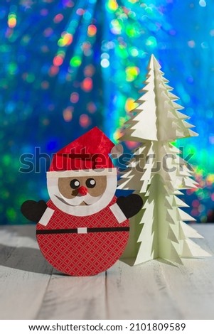 Santa Claus and white tree made with recycled paper and blurred lights in the background. Happy new year and merry Christmas. Holiday card