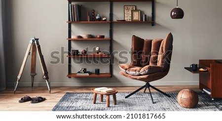 Stylish interior of living room with design brown armchair, wooden bookcase, pendant lamp, carpet decor, picture frames and elegant personal accessories in modern retro home decor. Template.