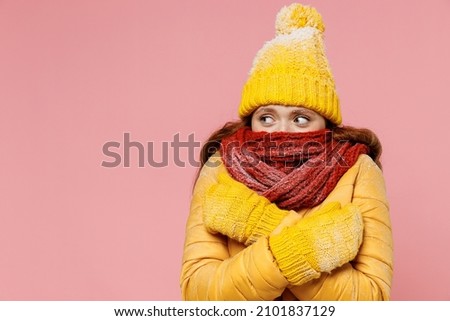 Young woman 20s years old wears yellow jacket hat mittens look aside cover hiding mouth with scarf wrapped neck hold hands crossed around isolated on plain pastel light pink background studio portrait Royalty-Free Stock Photo #2101837129