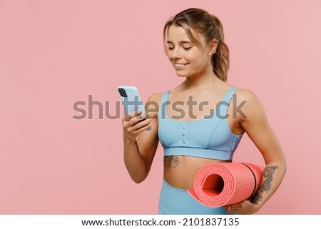 Young happy strong sporty athletic fitness trainer instructor woman wear blue tracksuit spend time in home gym hold use mobile cell phone isolated on pastel plain pink background Workout sport concept