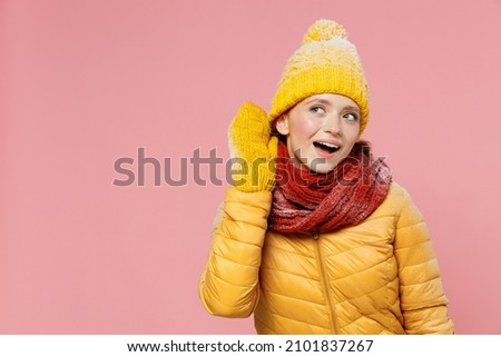 Curious nosy fun exultant energetic young woman 20s years old wears yellow jacket hat mittens try to hear you overhear listening intently isolated on plain pastel light pink background studio portrait