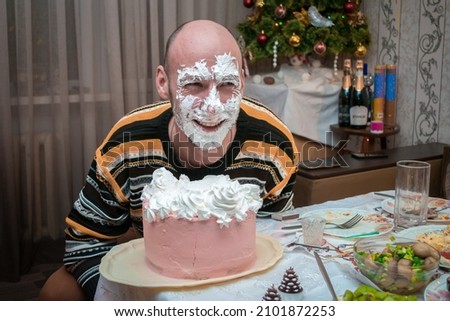The man fell face down on the cake. The guy licks the cream off the cake.
