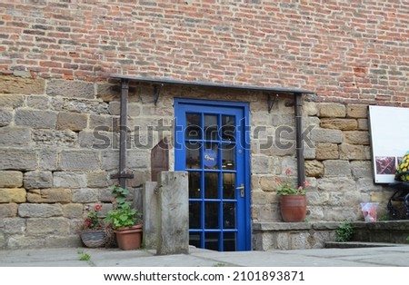 Low entrance to the old building made of stone blocks and red bricks - the blue door leads to the basement converted into usable space (the sign "open" in the door)