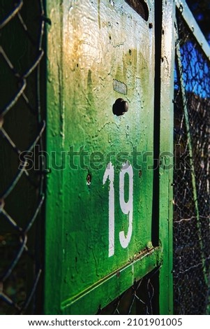 Sign with a house number that is very old and the green paint is already peeling off.
