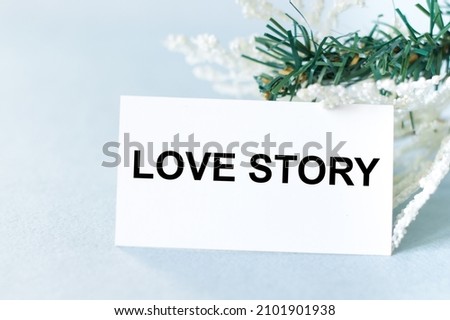 Love story text on the card next to spruce branches on a blue background. Valentines Day card