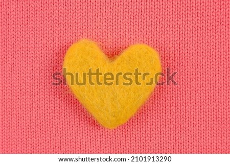 A yellow heart made of wool lies on a pink knitted background.Handmade concept, needlework, favorite hobby, sale of yarn for knitting.Cozy background for Valentine's Day greeting cards
