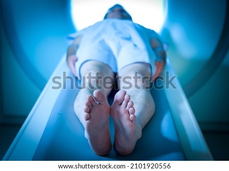 Unrecognizable male patient dressed in a hospital gown laying down ready to take a CT Scan at a hospital, with his feet as the main focal point. Royalty-Free Stock Photo #2101920556