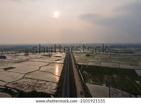 drone shot aerial view top angle sunset photo of train railway track running through Lake agricultural paddy fields in rural India Tamilnadu madurai turquoise blue water beautiful scenery 