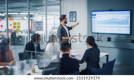 Diverse Modern Office: Motivated Businessman Leads Business Meeting with Managers, Talks, uses Presentation TV with Statistics, Chart Growth, Big Data. Digital Entrepreneurs Work on e-Commerce Project Royalty-Free Stock Photo #2101929379