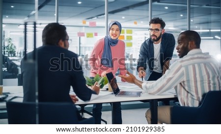 Diverse Modern Office: Muslim Businesswoman Wearing Hijab and Stylish Hispanic Entrepreneur Lead Business Meeting, Use Laptop, Talk, Brainstorm with Managers. Young Professionals on e-Commerce Project Royalty-Free Stock Photo #2101929385