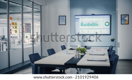 Modern Empty Meeting Room with Big Conference Table with Various Documents and Laptops on it, on the Wall Big TV with Big Data Analysis, Charts and Infographics. Contemporary Designed Work Environment Royalty-Free Stock Photo #2101929406