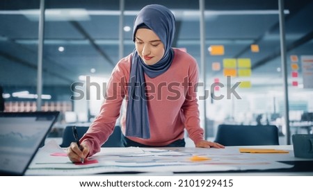 Modern Office: Motivated Muslim Businesswoman Wearing Hijab Works on Engineering Project, Does Document and Blueprints Analysis. Empowered Digital Entrepreneur Works on e-Commerce Startup Project Royalty-Free Stock Photo #2101929415