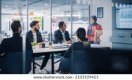 Multi-Ethnic Office Conference Room. Muslim Female CEO Wearing Hijab does Presentation for Group of Managers Talk, Use TV Infographics, Statistics. Businesspeople Brainstorm eCommerce Growth Strategy Royalty-Free Stock Photo #2101929421
