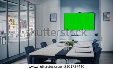 Modern Empty Meeting Room with Big Conference Table with Various Documents and Laptops on it, on the Wall Big TV with Green Chroma Key Screen. Contemporary Scandinavian Style Designed Work Environment