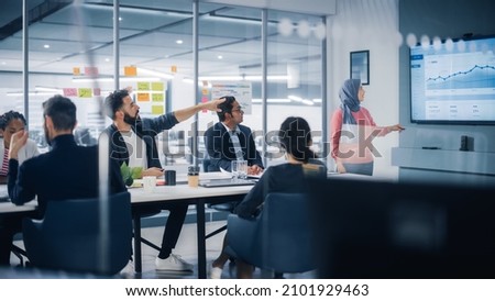 Multi-Ethnic Office Conference Room. Muslim Female CEO Wearing Hijab does Presentation for Group of Managers Talk, Use TV Infographics, Statistics. Businesspeople Brainstorm eCommerce Growth Strategy Royalty-Free Stock Photo #2101929463