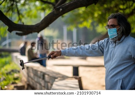 smart old man in mask recording his own activity on mobile phone