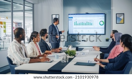 Multi-Ethnic Office Conference Room. Brilliant Indian Male CEO does Presentation for Multi-Ethnic Group of Managers Talking, Using TV Infographics, Statistics, Graphs. Innovative Businesspeople Royalty-Free Stock Photo #2101930978