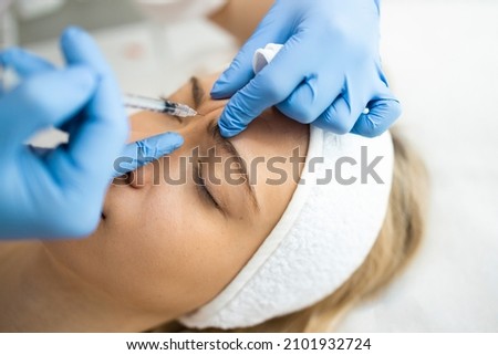 Beautician makes botox injections in the area between the eyebrows. Anti aging procedure Royalty-Free Stock Photo #2101932724