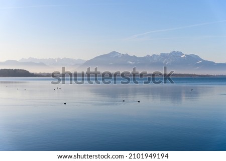 Calm Chiemsee in winter with ducks mountains and clear sky fog