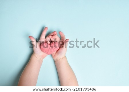 Children's hands hold a small pink knitted heart on a blue background. Love. Organ donation.Flat position, top view. valentine's day.