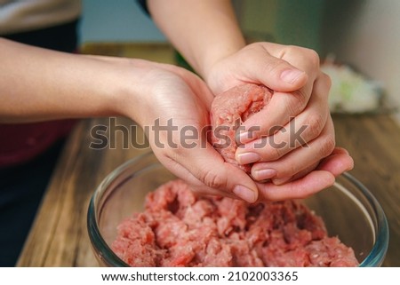 Close-up of a woman's hands preparing ground beef to make hamburgers, the meat is still raw and she is adding the ingredients, nice atmosphere in the kitchen. Royalty-Free Stock Photo #2102003365