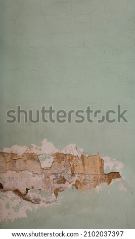 Old light green painted dirty scratched shabby stucco wall and yellow brickwork in the crack. Vertical photo background