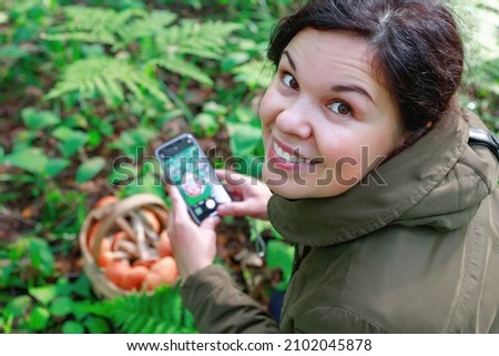 Woman in the forest takes pictures of a basket full of red capped boletus mushrooms. Summer woodland nature park walk, gourmet hobby.