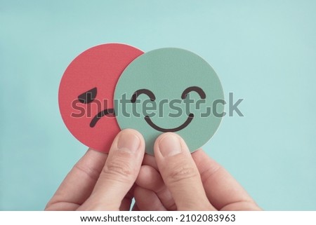 Hands holding sad face hiding behind happy face, bipolar and depression, mental health, split personality,  mood change concept Royalty-Free Stock Photo #2102083963