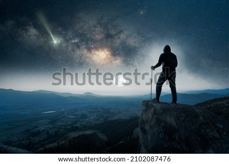 silhouette of a hiker on the top of the mountain staring the Milky Way and shooting star on the horizone