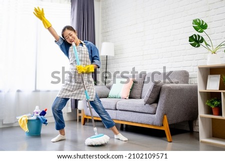 Happy young Asian woman cleaning her home, singing at mop like at microphone and having fun, free space.  Royalty-Free Stock Photo #2102109571