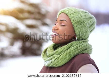 Portrait of beautiful attractive happy girl young black African Afro American woman is enjoying good cold frosty sunny day at winter snow park with eyes closed, breathing deeply deep fresh air smiling Royalty-Free Stock Photo #2102157619