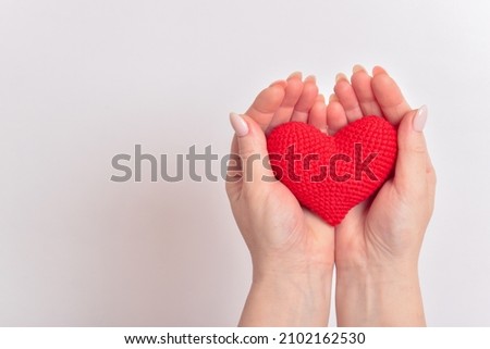 A red knitted heart in the palms of a girl with a beautiful manicure. Love. Organ donation. Pregnancy. Copy space.