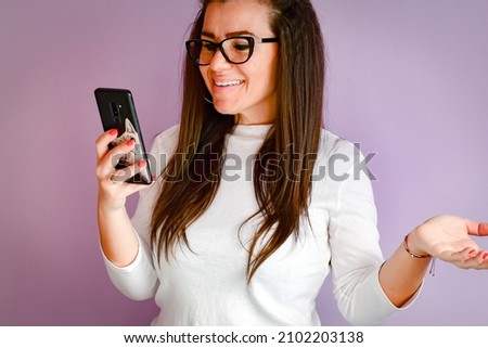Cheerful Happy smiling woman in eyeglasses looking at the phone  reading a Message ,checking social media, shopping online,  ordering delivery  against pink wall, connected to high speed internet
