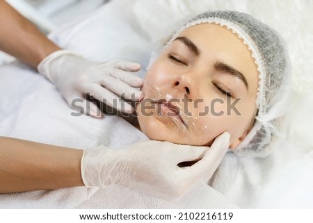 Professional permanent makeup artist applying anesthetic on client's lips before lip blushing procedure Royalty-Free Stock Photo #2102216119