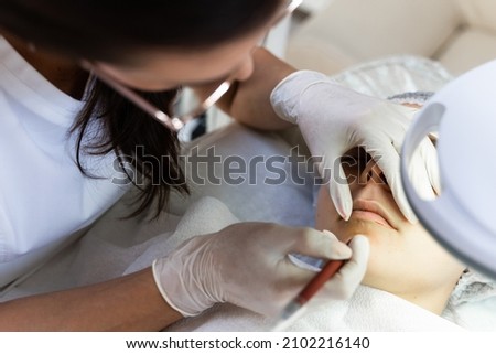 Professional permanent makeup artist and her client during lip blushing procedure Royalty-Free Stock Photo #2102216140
