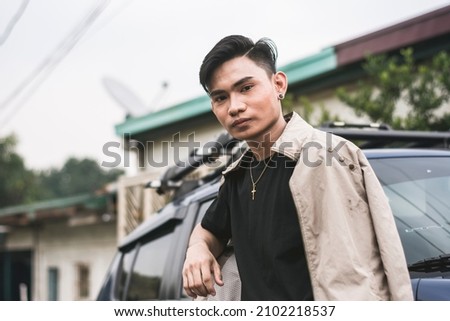 A young successful asian man posing in front of his blue car. Royalty-Free Stock Photo #2102218537