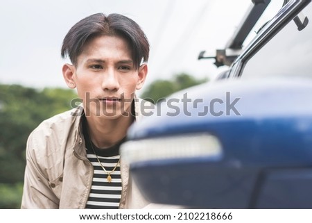 A vain main checks his reflection on the side mirror of a car. Outdoor scene. Royalty-Free Stock Photo #2102218666