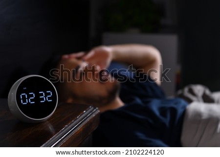 Depressed young Asian man lying in bed cannot sleep from insomnia. focus on clock Royalty-Free Stock Photo #2102224120