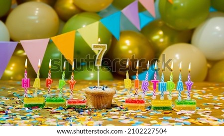 Happy birthday greeting card to a 7 year old child, birthday cupcake with candles and birthday decorations on the background