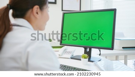 back view of asian female doctor works and uses computer with green screen monitor in hospital