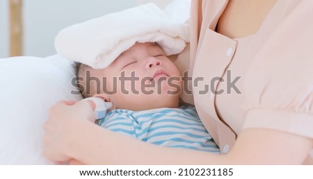 authentic shot of asian baby has fever and his mother checks temperature by thermometer on sofa in close up Royalty-Free Stock Photo #2102231185