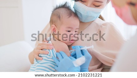 authentic shot of asian mother wearing face mask holds her baby for vaccinated by doctor Royalty-Free Stock Photo #2102231221